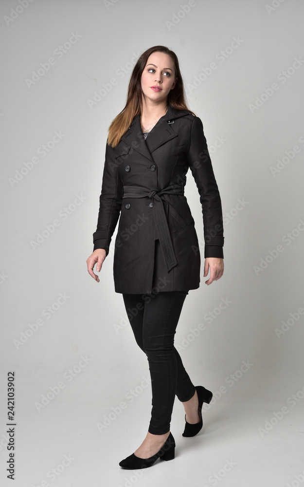 full length portrait of a brunette girl wearing long black coat, standing pose on grey studio background. full length portrait of a brunette girl wearing long black coat, standing pose on grey studio background.