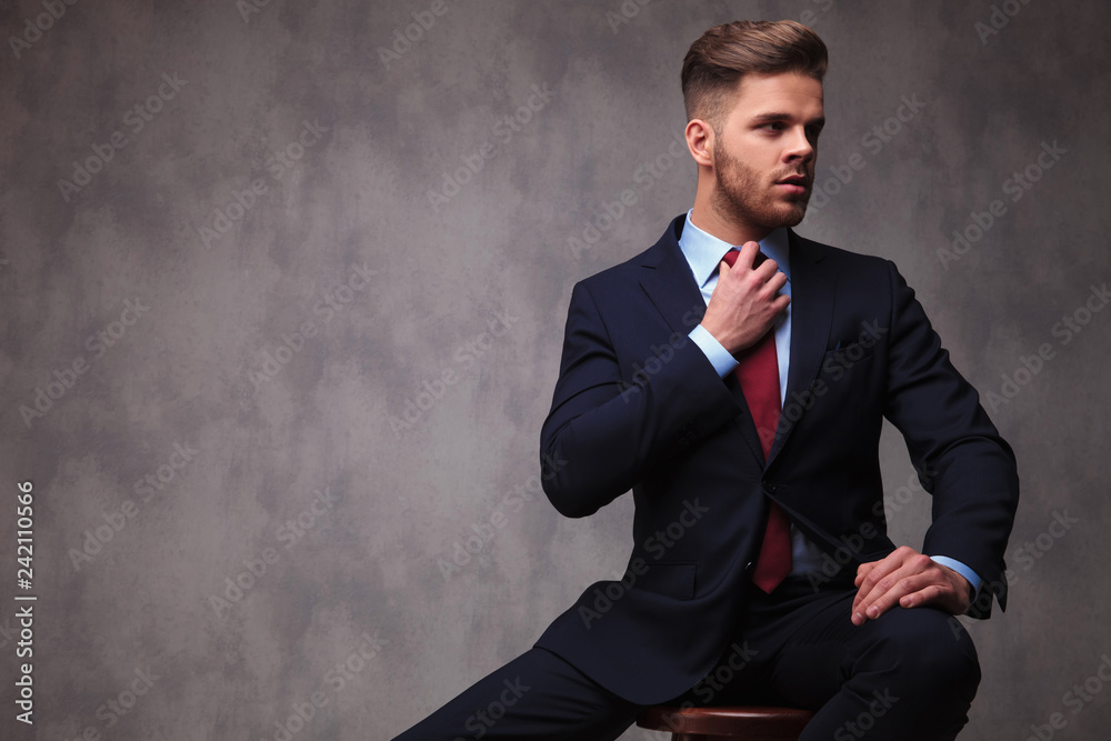 seated businessman looks to side while fixing red bowtie seated businessman looks to side while fixing red bowtie