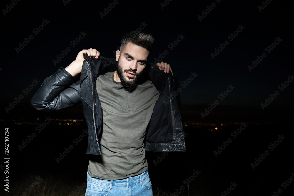 portrait of man holding leather jacket collar standing outdoor