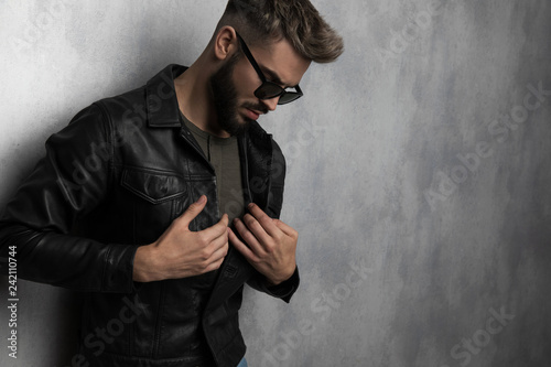 portrait of man buttoning leather jacket while looking down