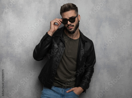 portrait of seductive relaxed man in leather jacket arranging sunglasses