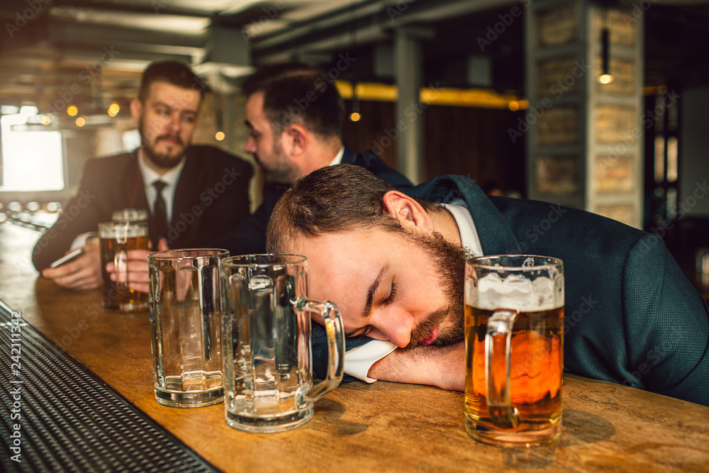 Tired young man in suit sleep on bar counter. He is drunk. there are ...