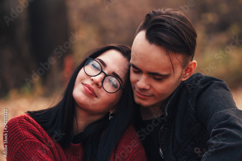 young man and young woman are sitting on a plaid in an autumn forest