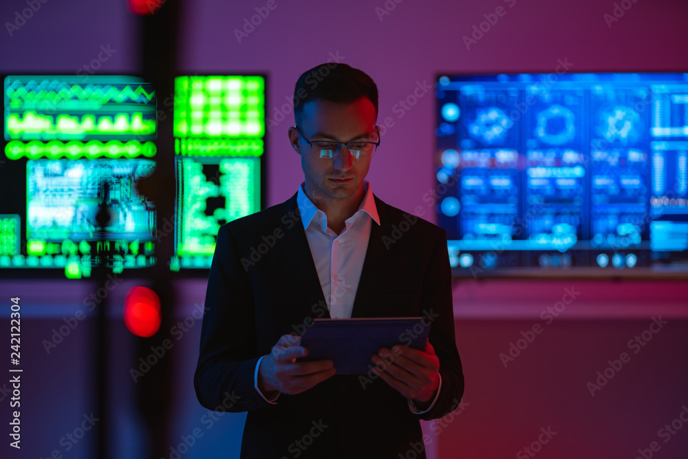 Fototapeta premium The businessman with a tablet standing on screens background