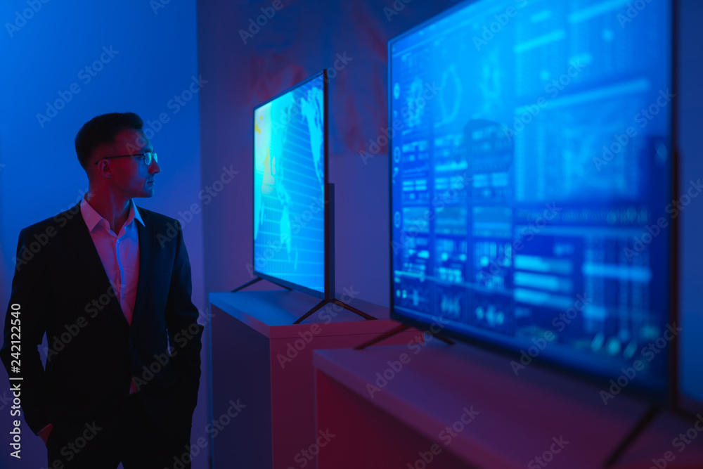 Fototapeta premium The businessman standing near screens in the dark room