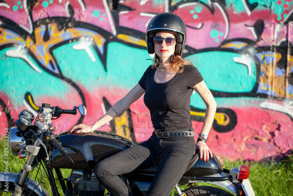Mujer de negro con moto junto a grafiti Mujer de negro con moto junto a grafiti