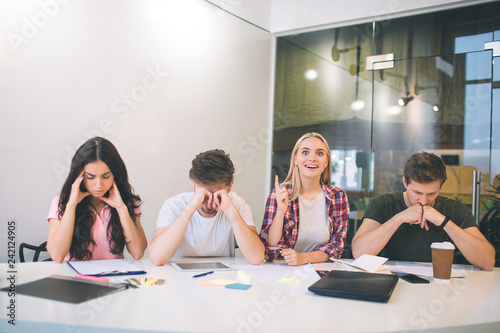 Picture of young blonde woman smiling. She point up. Model got an idea. Other people have brainstorming. They think and try to be concentrated.