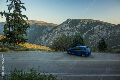 Fototapeta Naklejka Na Ścianę i Meble -  economy blue car stop on side of road on mountain highland scenery landscape in evening twilight before sunset