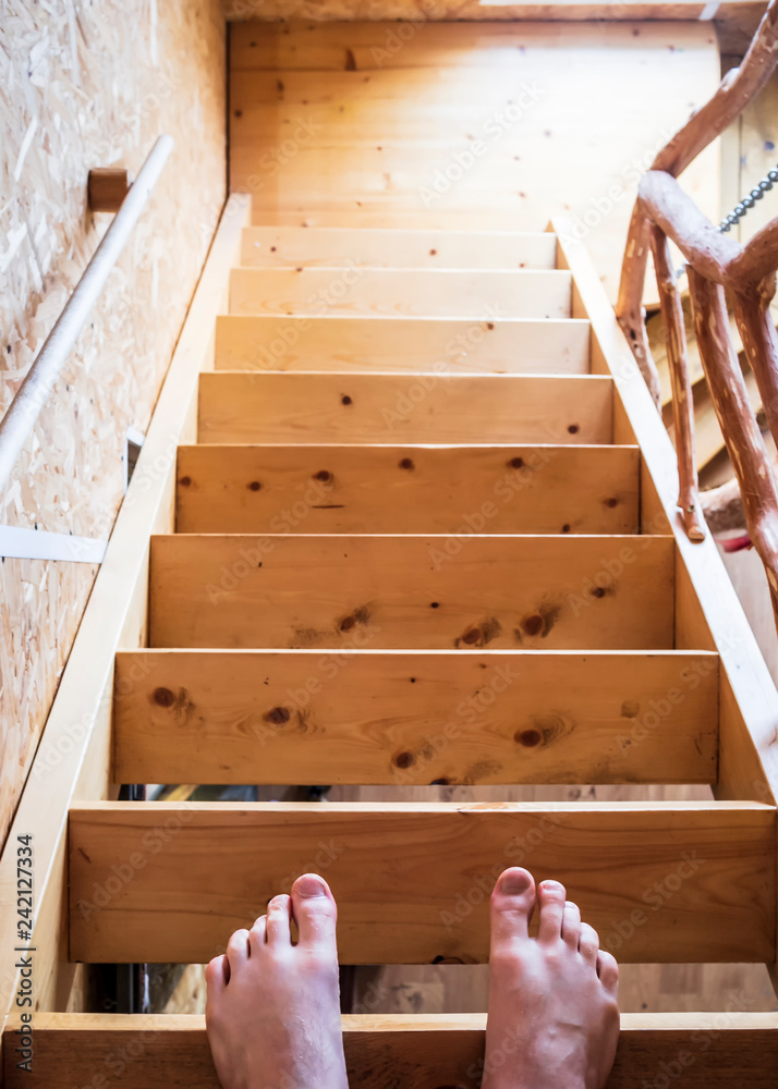 The legs of a man stand on the top step of a wooden staircase, in a house. The legs of a man stand on the top step of a wooden staircase, in a house.