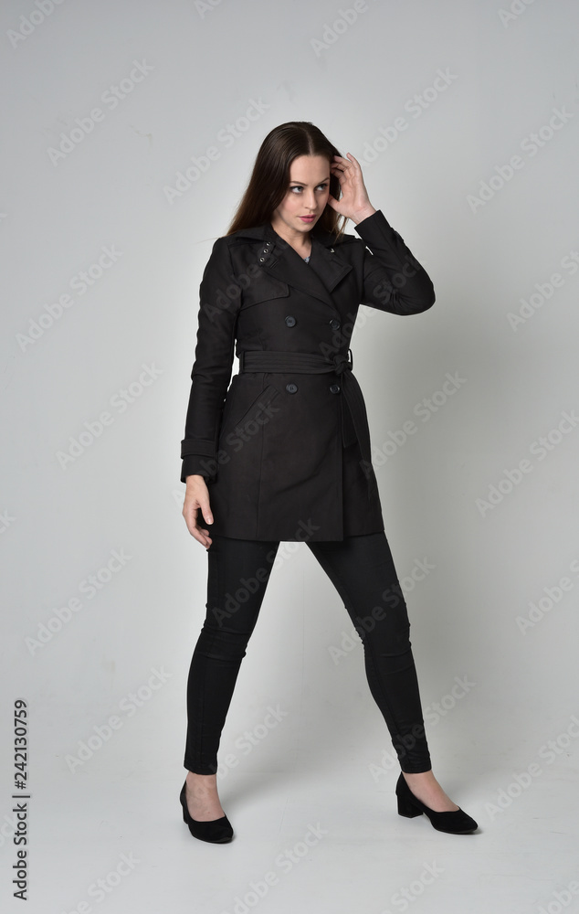 full length portrait of a brunette girl wearing long black coat, standing pose on grey studio background. full length portrait of a brunette girl wearing long black coat, standing pose on grey studio background.