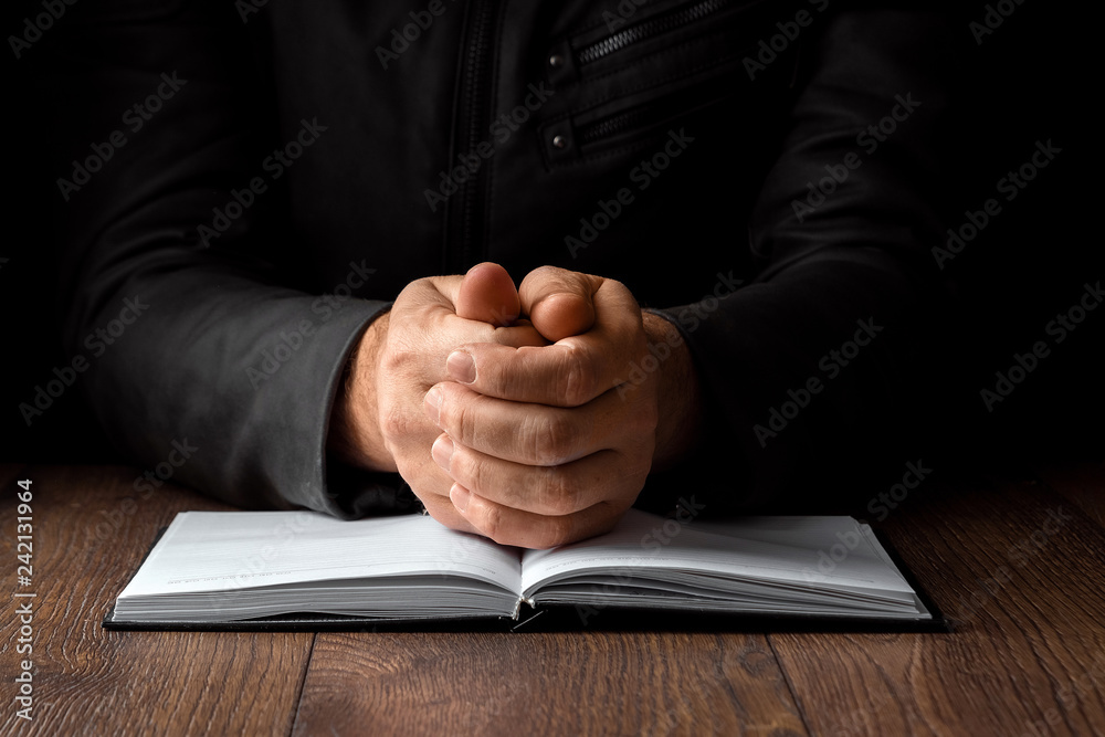 Obraz premium Men's hands in prayer on a black background. The concept of faith, prayer, mourning, forgiveness, confession.