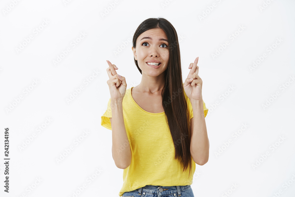 Opimistic and hopeful charming slim woman with long dark hair biting lip and smiling faithful crossing fingers for good luck looking up like believer praying and waiting for miracle or wish come true Opimistic and hopeful charming slim woman with long dark hair biting lip and smiling faithful crossing fingers for good luck looking up like believer praying and waiting for miracle or wish come true