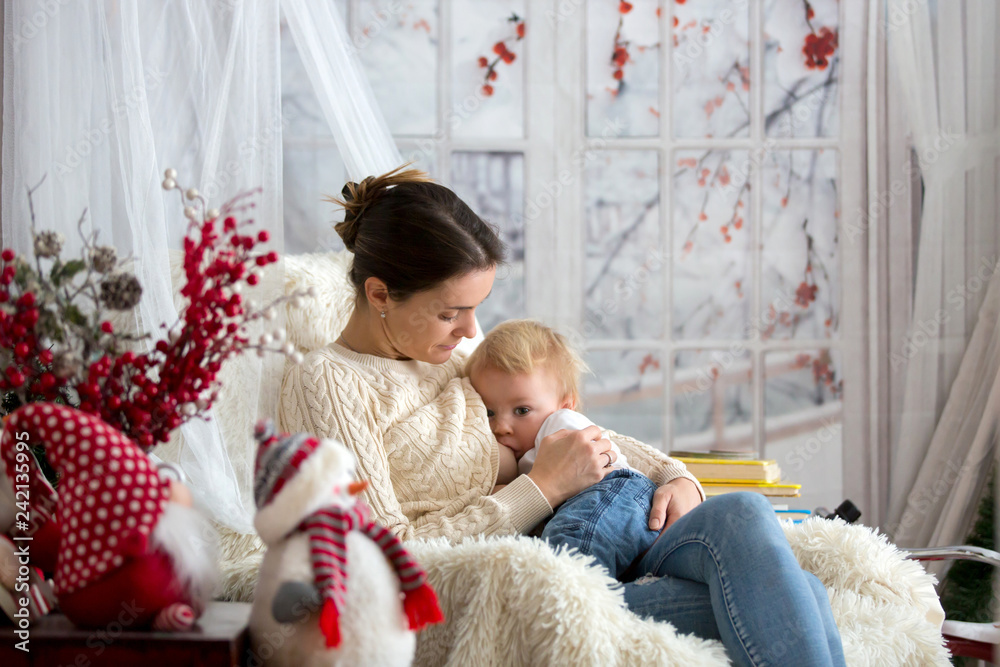 Mother breastfeeding her toddler son sitting in cozy armchair, wintertime. Mother breastfeeding her toddler son sitting in cozy armchair, wintertime.
