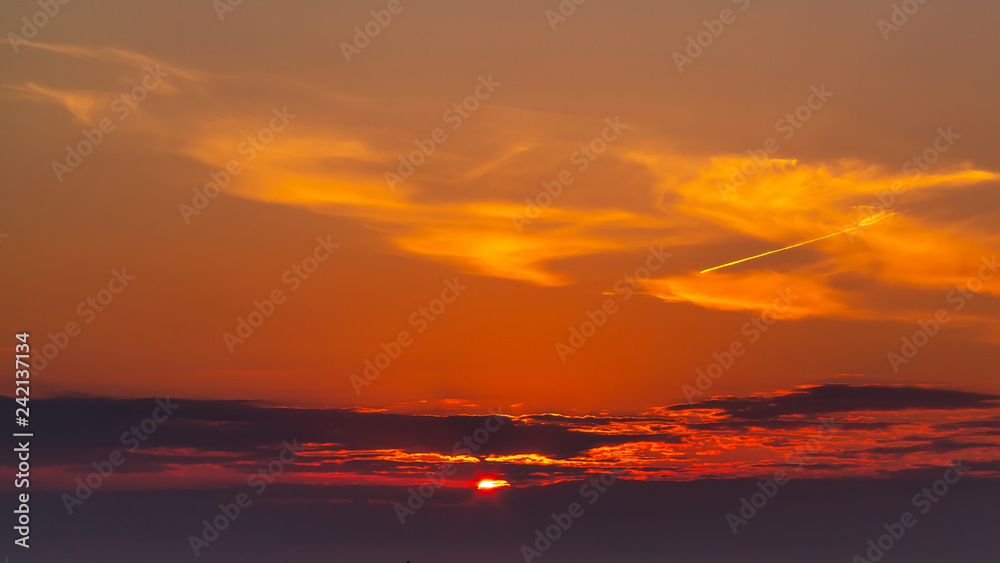 sky during a colorful, bright orange sunset, sun's rays make their way through the clouds