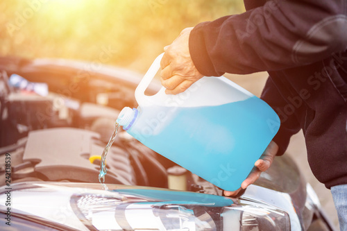 man refills windshield wiper water on a car