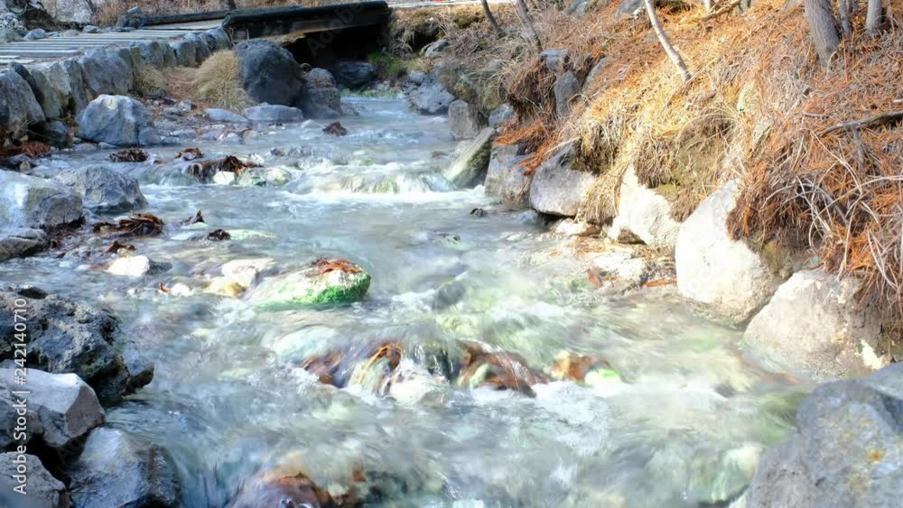 Waterfall from hot spring sources collected into a pool and hot water running down the valley in a warm stream in Kusatsu Onsen hot spring, Japan
