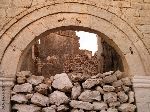 Pile of rocks blocking arched entrance with ruined building walls in the background, Qeparo, Albania photo