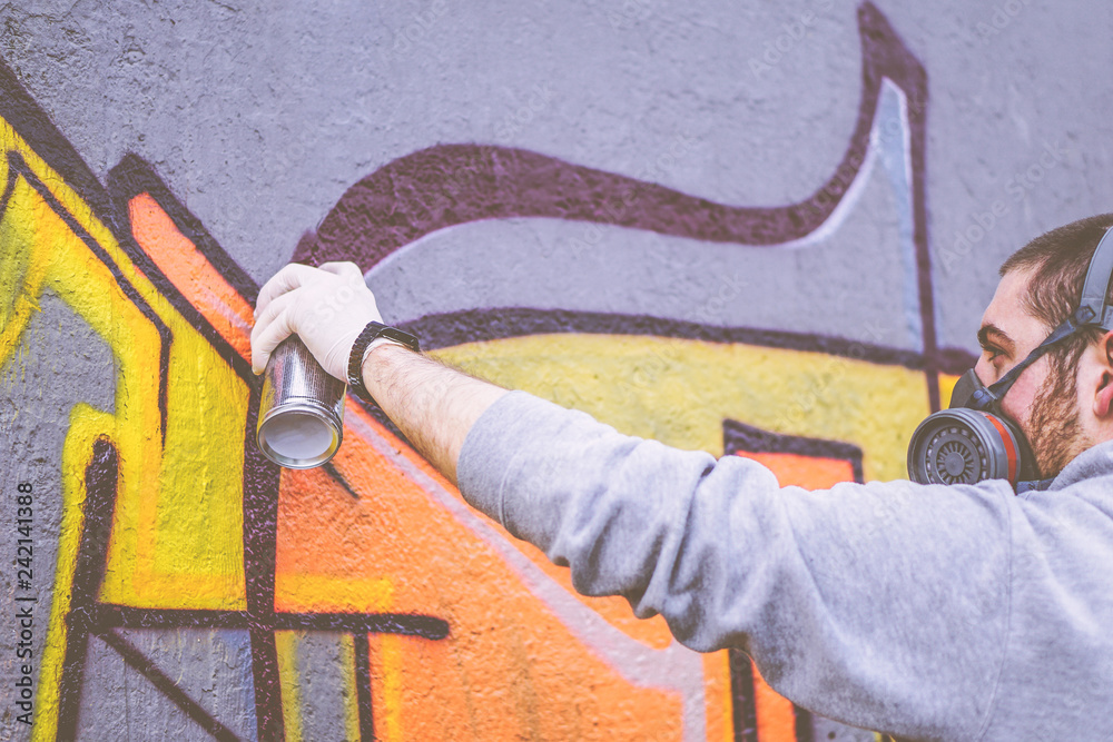 Obraz premium Artysta uliczny malujący kolorowym sprayem graffiti na ścianie na zewnątrz - Miejski mężczyzna wykonujący fototapety - Koncepcja nowoczesnej sztuki współczesnej - Skoncentruj się na dłoni