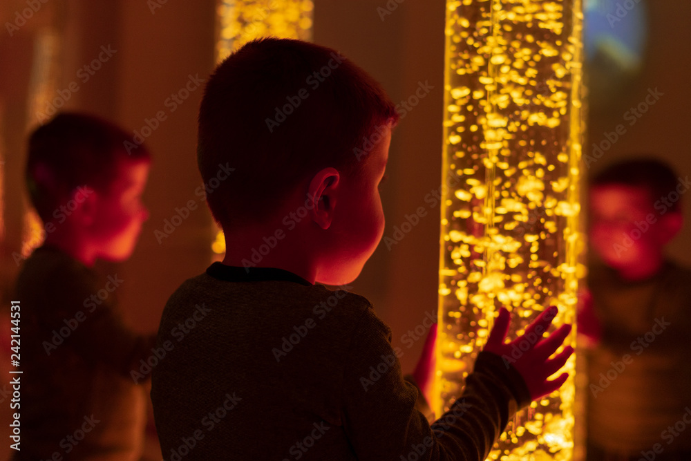 Child in therapy sensory stimulating room, snoezelen. Child interacting with colored lights bubble tube lamp during therapy session. Child in therapy sensory stimulating room, snoezelen. Child interacting with colored lights bubble tube lamp during therapy session.