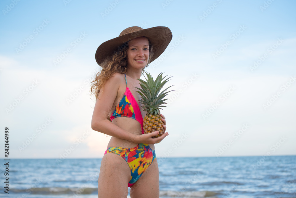 Beautiful woman holding pineapple and having fun on the beach