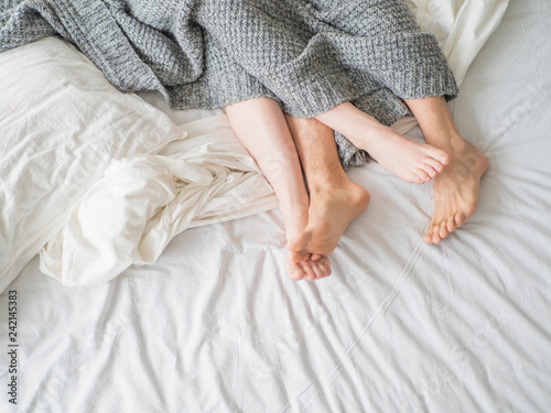 Close up of male and female feet on a bed - Loving couple under grey blanket in the bedroom - Concept of sensual and intimate moment of lovers. photo