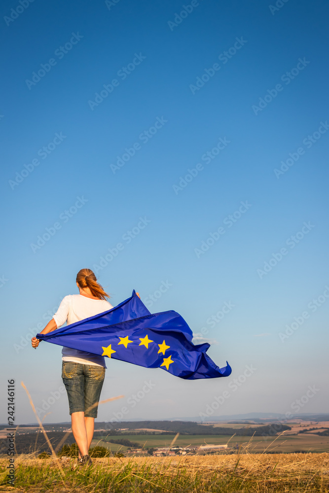 EU flag in female hands. Woman holding waving European Union flag against blue sky - obrazy, fototapety, plakaty 
