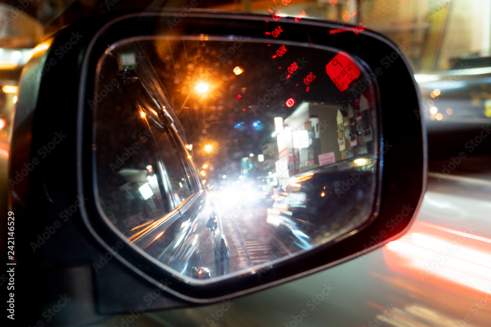 Mirror view of car at night. Bokeh image of lighting in the glass. Fast of other cars with red light. Reflection of the red speedometer curtain. Mirror view of car at night. Bokeh image of lighting in the glass. Fast of other cars with red light. Reflection of the red speedometer curtain.