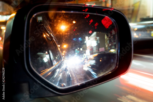 Mirror view of car at night. Bokeh image of lighting in the glass. Fast of other cars with red light. Reflection of the red speedometer curtain. © thongchainak