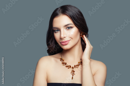 Jewelry model girl. Brunette woman with makeup, long hair and amber necklace and earrings on blue background