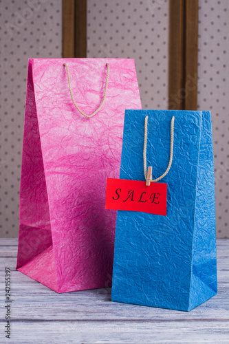 Pink and blue paper shopping bags. Two colorful carrier gift bags and red card with inscription sale, vertical image.