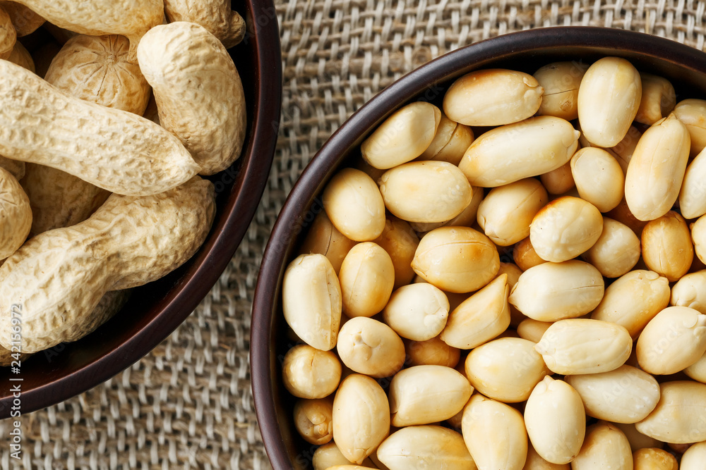 Peanuts in the shell and peeled close-up in cups. Roasted peanuts in their shells and peeled against a brown cloth.