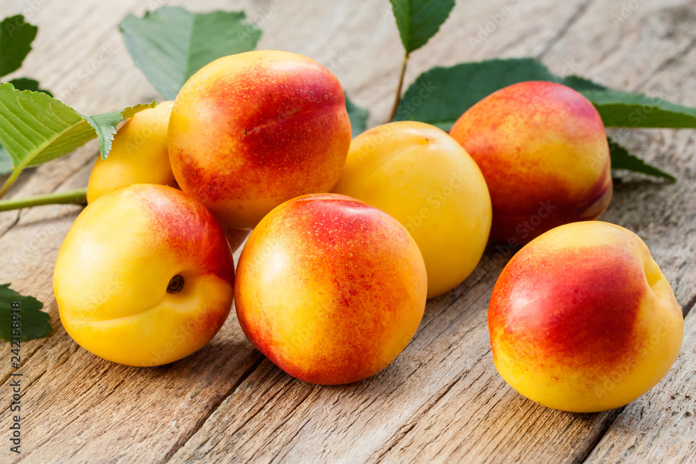 Fresh sweet nectarines with fresh green leaves on wooden background in the garden, ripe peaches, organic gardening Fresh sweet nectarines with fresh green leaves on wooden background in the garden, ripe peaches, organic gardening