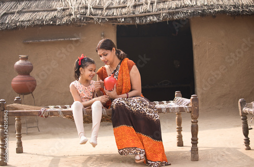 Mother with daughter holding piggy bank at village