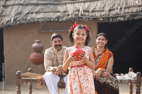 Indian little girl holding piggy bank in front of parents