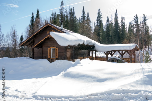 A wooden house stands among white snowdrifts against a background of spruce forest.