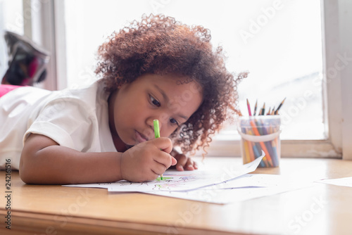 Little toddler girl laying down concentrate on drawing. Mix African girl learn and play in the pre-school class. Children enjoy hand writing. 3 years girl enjoy playing at nursery.