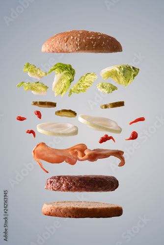Beef burger floating with bacon onion and pickles gray background