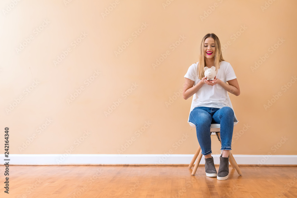 Fototapeta premium Young woman with a piggy bank in a chair