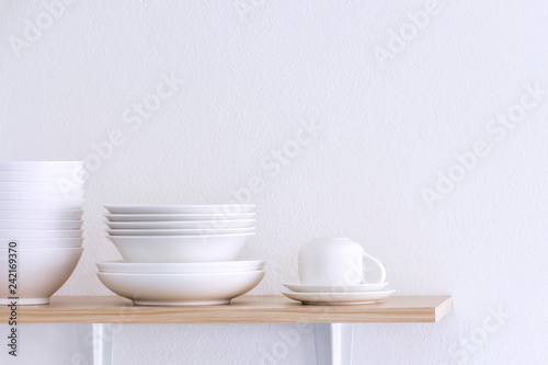 Wooden shelf template isolated on white wall background which on set stacked white bowls and plates as items tableware for decorated interior or montage of your product on shelf with copy space.