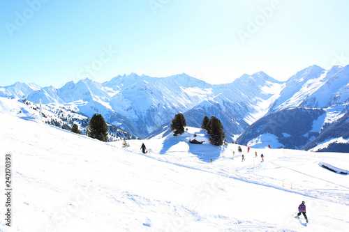 People enjoying skiing on prepared slopes in the Alps on sunny day. Beautiful snowy trees in the mountains. Perfect winter holidays destination for family in modern comfortable Alpine ski resort.  © cromary