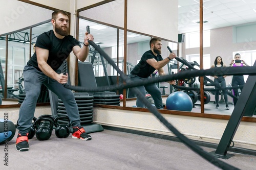 Athletic muscular bearded man exercising in the gym with battle ropes. Sport, training, people, healthy lifestyle concept.