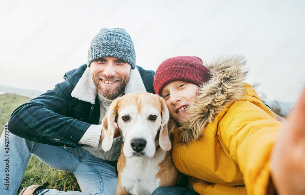 Father and son dressed in warm clothes taking a selfie photo with their best family member beagle dog