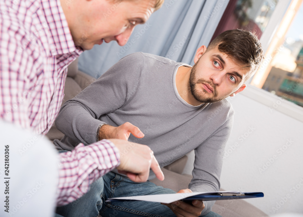 Fototapeta premium Upset man with friend looking at papers on sofa