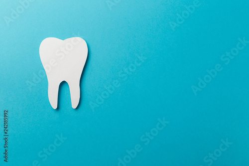 White tooth on blue background with copy space. Oral dental hygiene. Teeth whitening. Dental health concept. Oral care, teeth restoration. Dentist day concept. Flat lay. Top view. Pastel colors