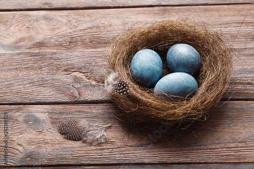 Three marble blue Easter eggs, in a nest with feathers on a wooden background. The Symbol Of Easter. Copy space