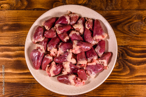 Ceramic plate with raw chicken hearts on wooden table. Top view