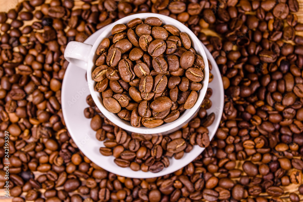 Fototapeta premium White cup filled with coffee beans on wooden table. Top view