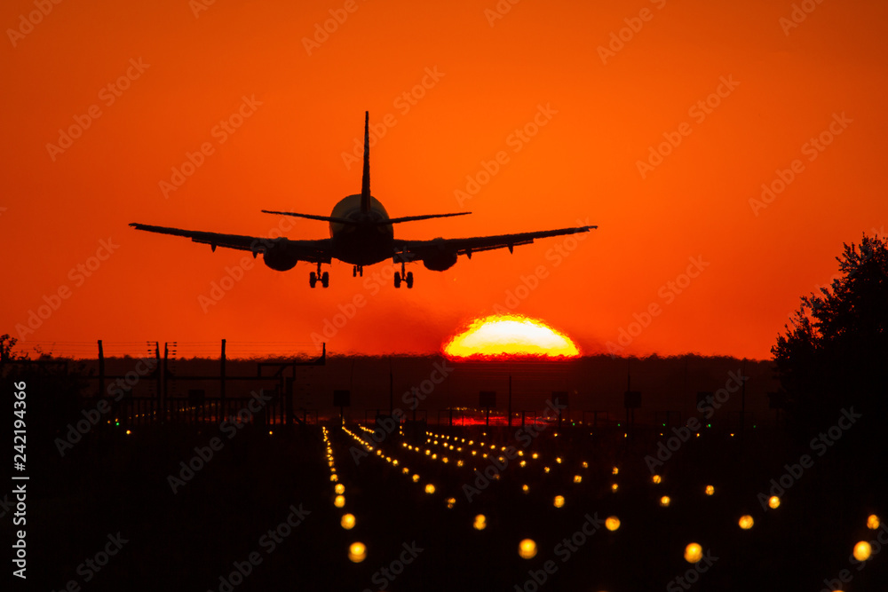 Silhouette of air plane landing on illuminated track at sunset with beautiful red sky and sun in background Silhouette of air plane landing on illuminated track at sunset with beautiful red sky and sun in background