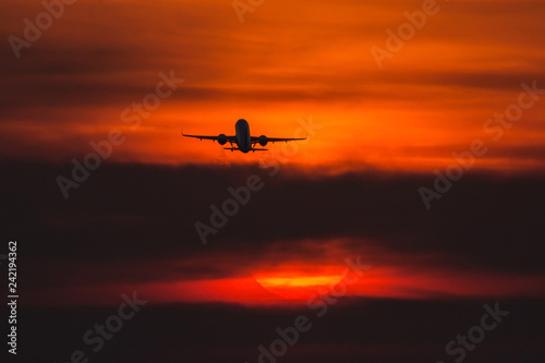 Fototapeta Naklejka Na Ścianę i Meble -  Air plane taking off at sunset near to the sun with beautiful red cloud in background