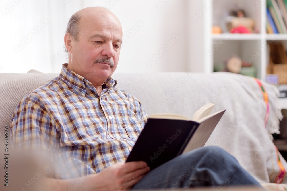 Senior man reading a book on his sofa Senior man reading a book on his sofa